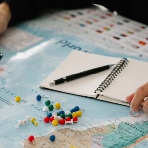 Close-up of hands planning a trip with map, pins, and notebook.