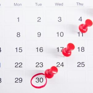 Close-up of a calendar with red push pins marking important dates, emphasizing deadlines.